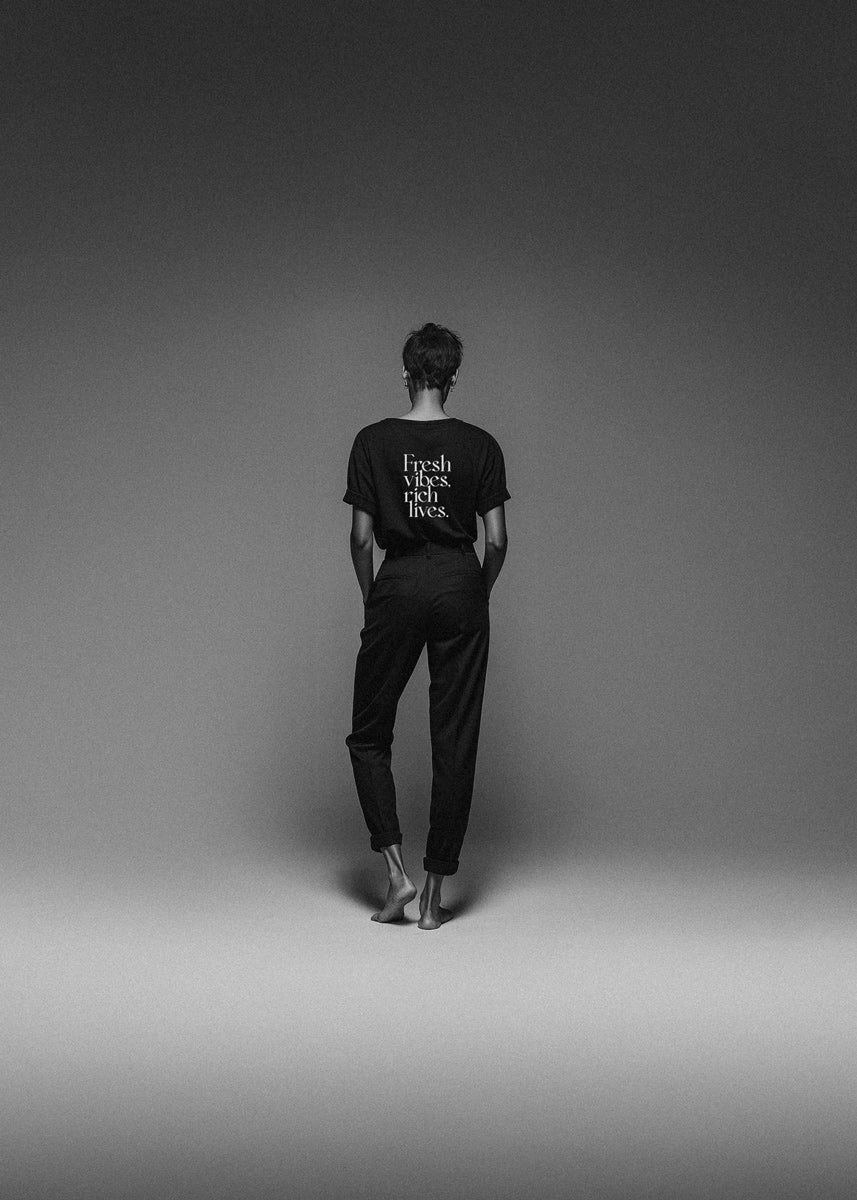 Person wearing a black t-shirt with text on the back, standing against a plain gray background