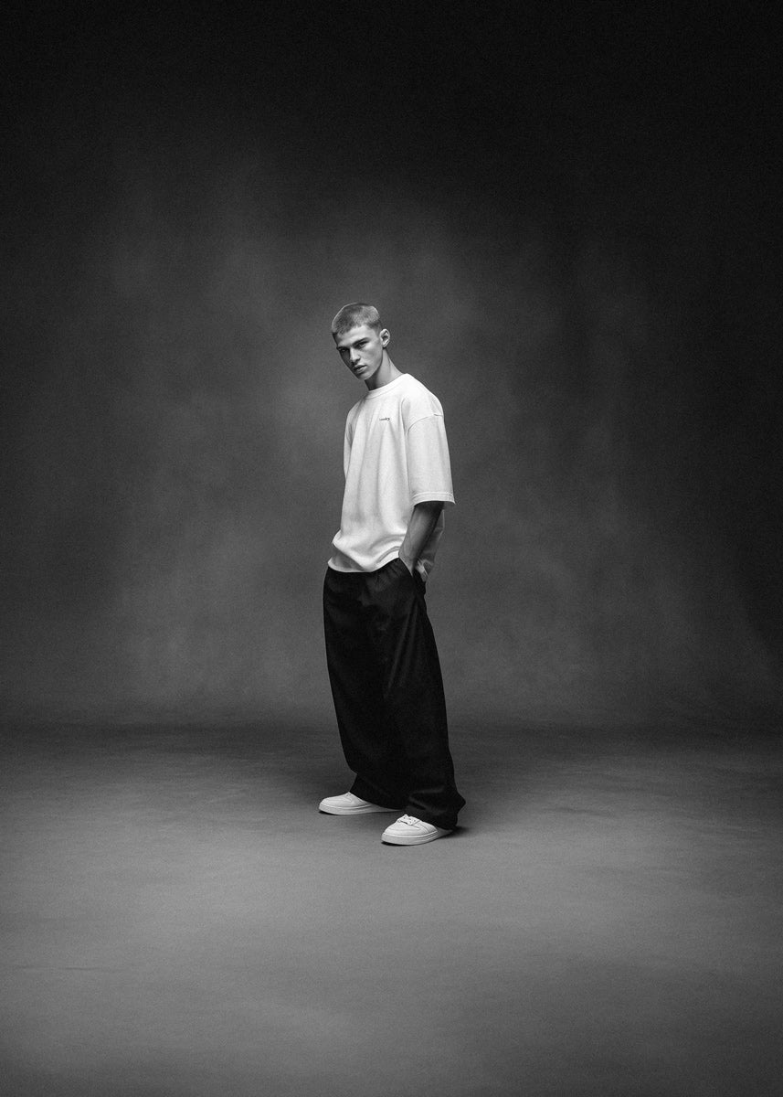 Person wearing a white t-shirt and black pants standing against a dark background