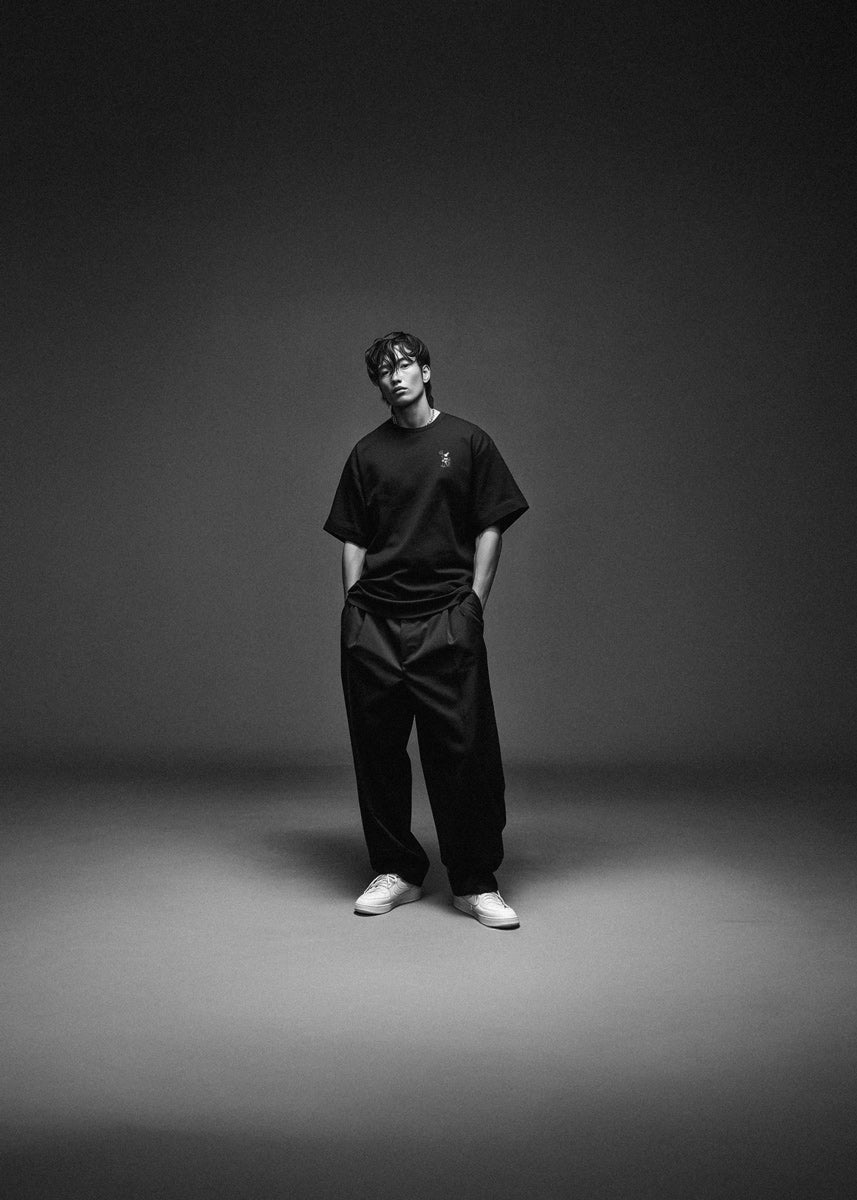 Person wearing a black t-shirt and pants standing against a dark background