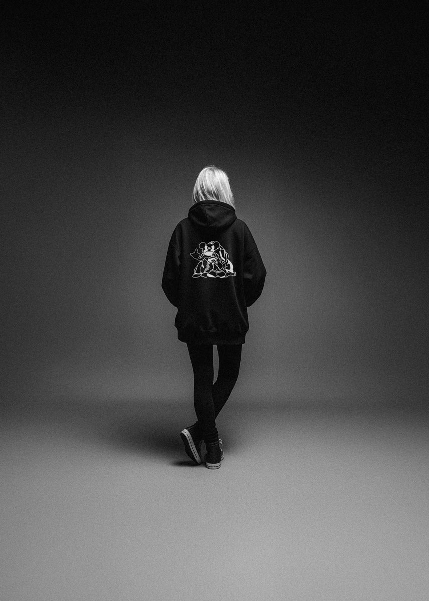 Person wearing a black hoodie with a logo on the back, walking away against a dark background