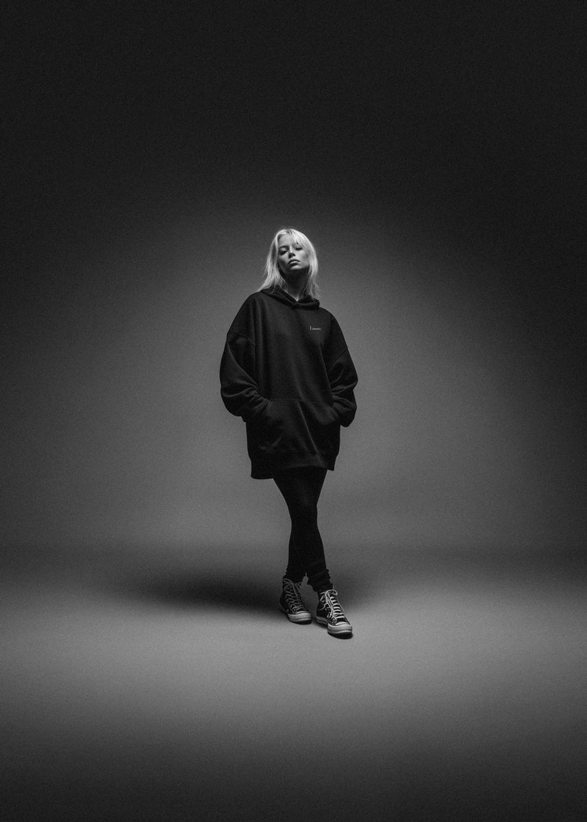 Person wearing a black hoodie and pants standing against a dark background