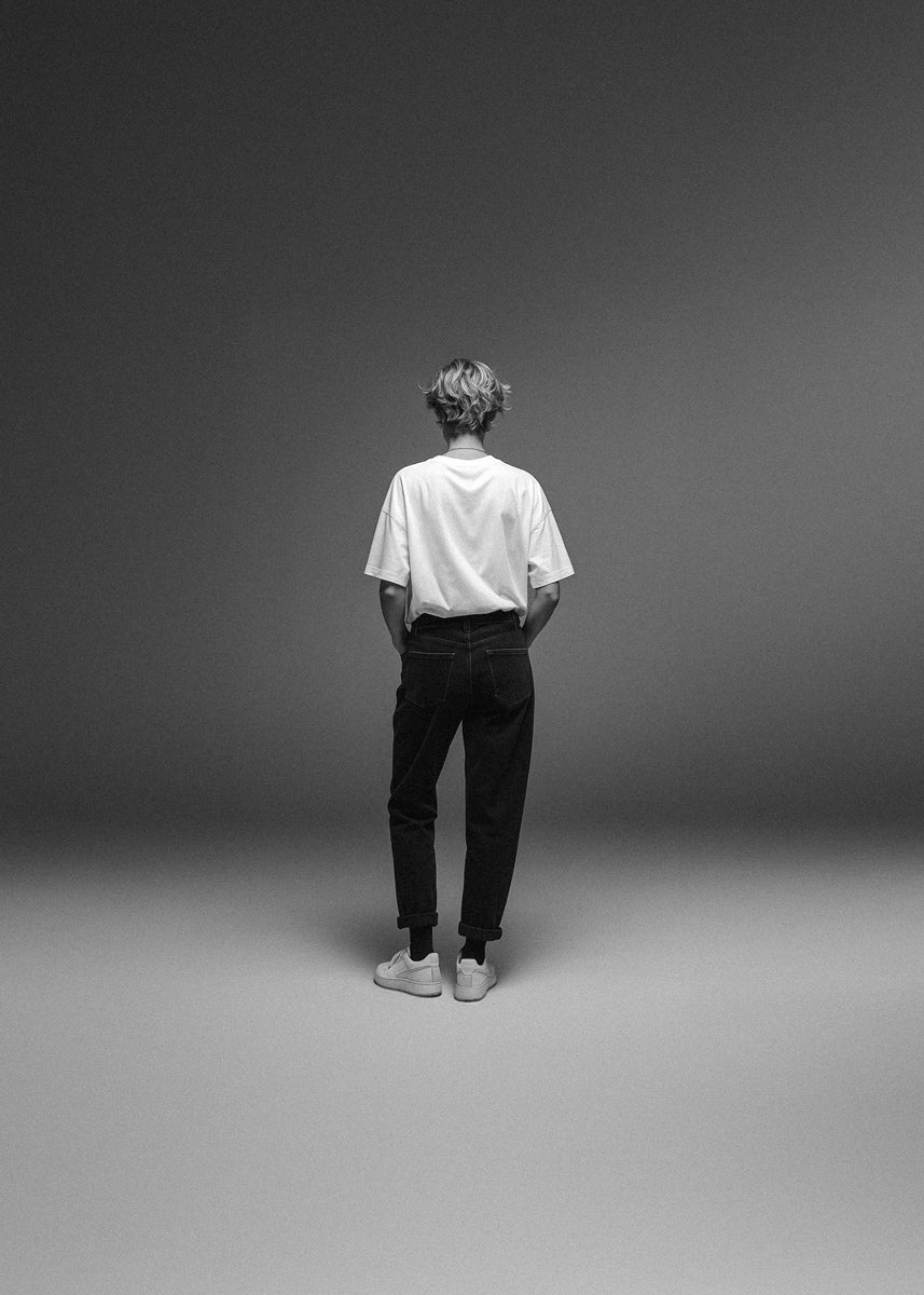 Person wearing a white shirt and black pants standing against a gray background